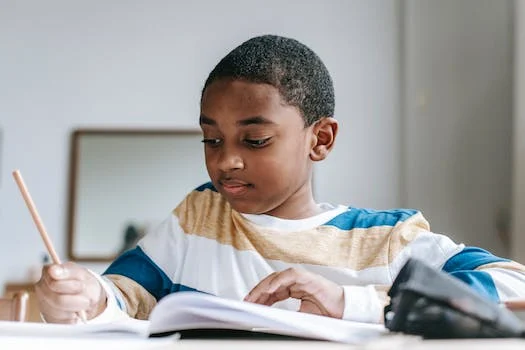 Ein Junge sitzt an einem Tisch und schreibt mit einem Bleistift, wobei er betont, wie wichtig Finanzwissen für die Sicherung der eigenen Zukunft ist.